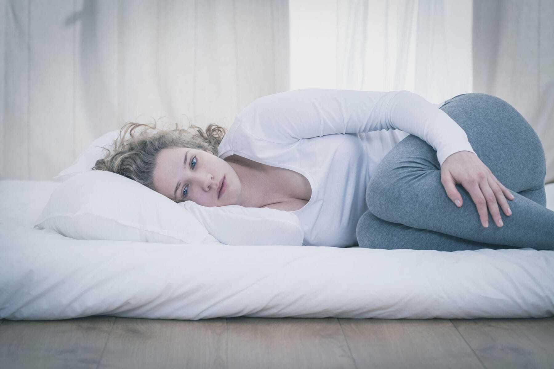 Upset woman laid in bed staring at the floor